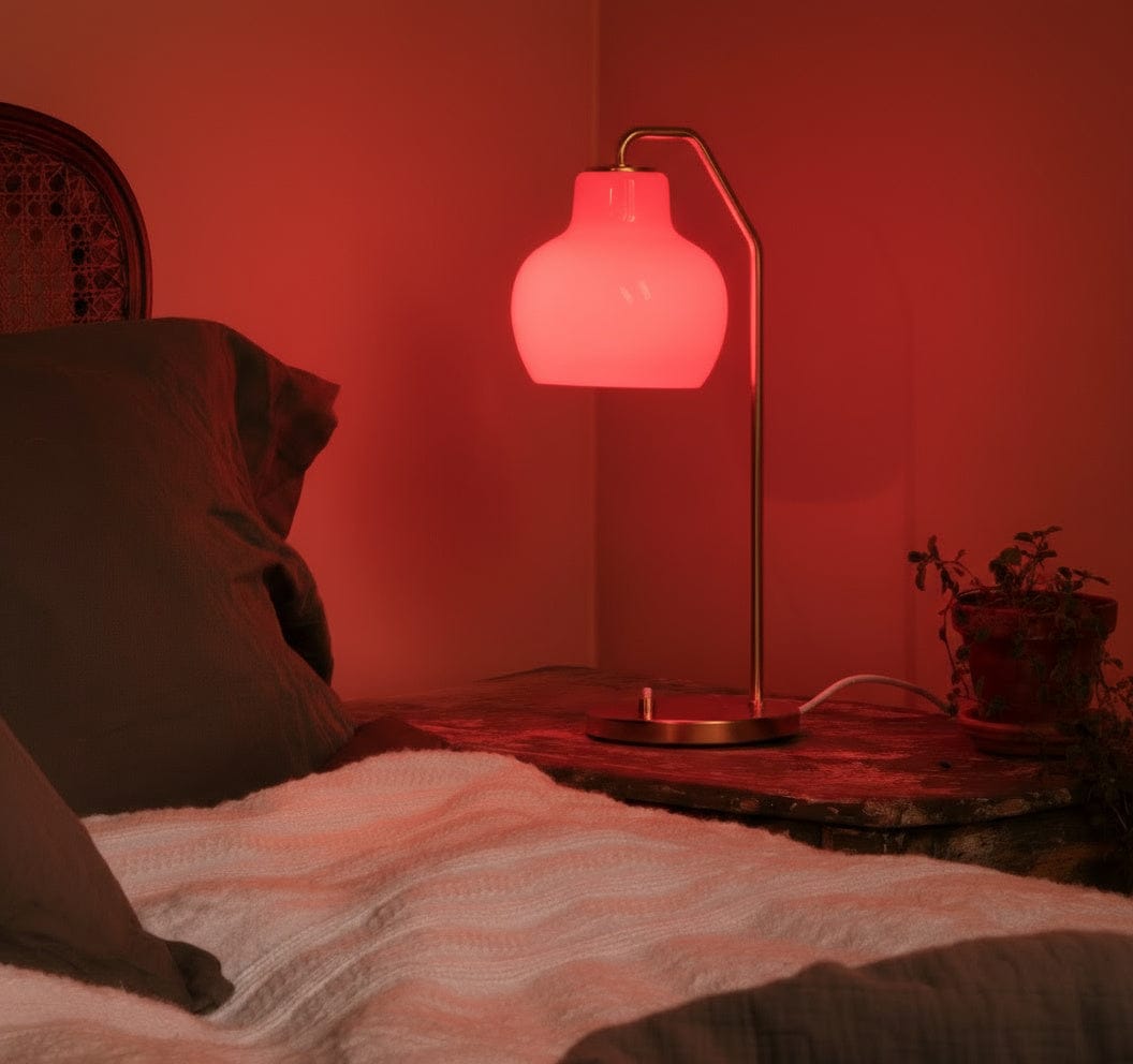 Red lamp on a bedside table with a warm glow in a bedroom setting.