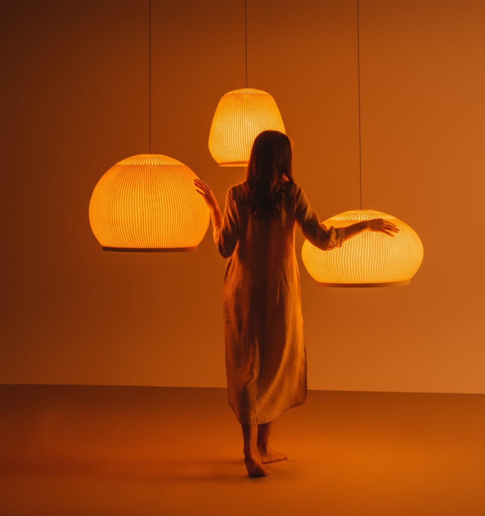 Person standing in a room with three hanging lamps casting a warm glow.