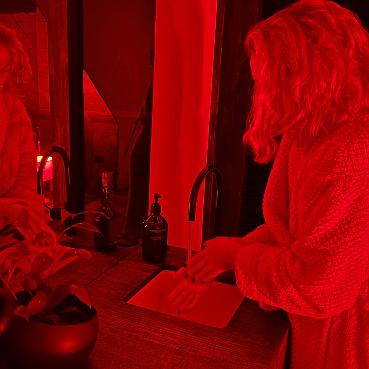 Person washing their hands at a bathroom basin late at night, the room lit only by a motion-activated red night light