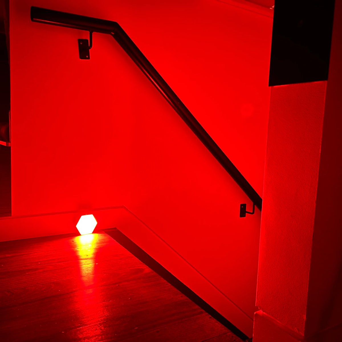 Motion-activated red night light at the foot of a staircase, casting red light across timber floorboards and up the handrail wall at night