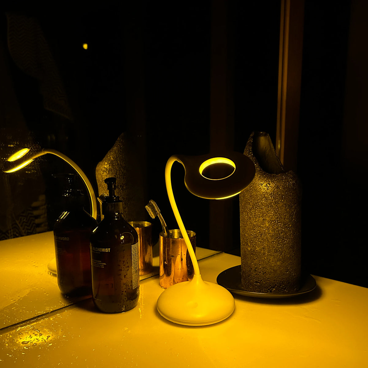 Blue blocking amber sleep lamp lighting a bathroom vanity at night, its warm amber glow falling across hand wash bottles and a toothbrush cup in an otherwise dark room